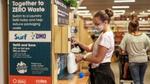 Woman filling a plastic bottle from an in-store refill machine that dispenses Surf and OMO products.