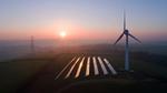 Aerial view of rural landscape showing wind turbine and solar panels in field.