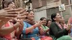 A group of South Asian women in colourful clothes sit on the floor smiling and clapping
