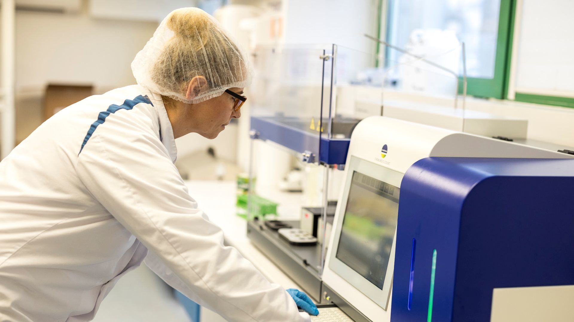 A factory worker in white coat and hairnet takes a close look at a computer.