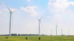 Wind turbines stand in a field with people watching them