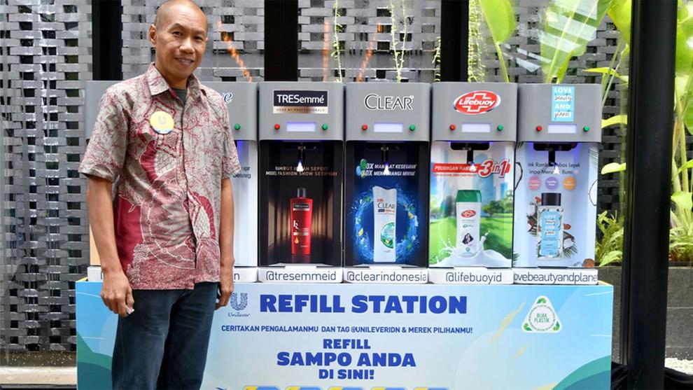 Man standing in front of Unilever’s in-store refill station in Indonesia. Machine has dispensers for products including TRESemmé, Clear and Lifebuoy.