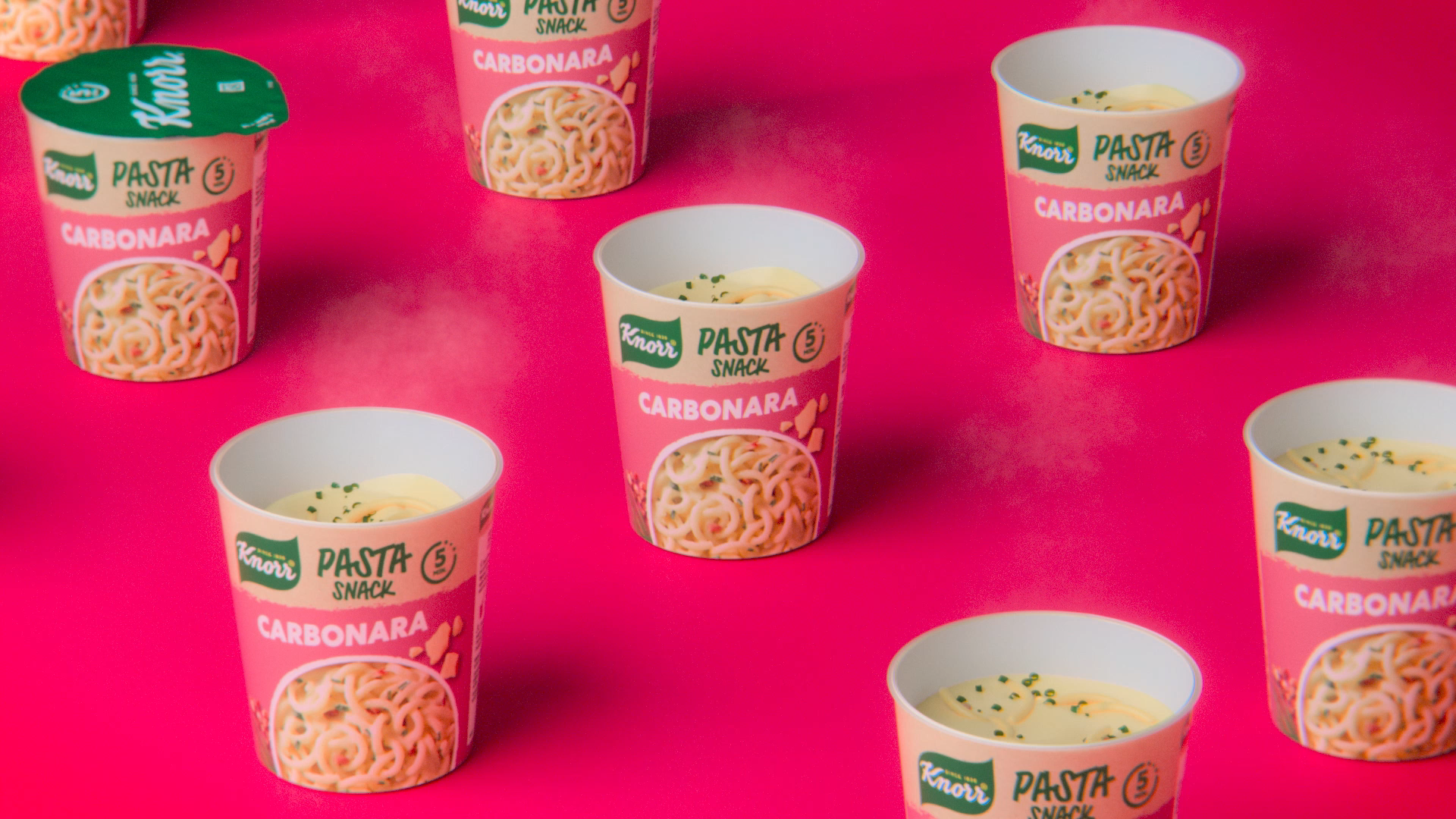 Six Knorr Carbonara Mini Meal pots set against a bright pink background.