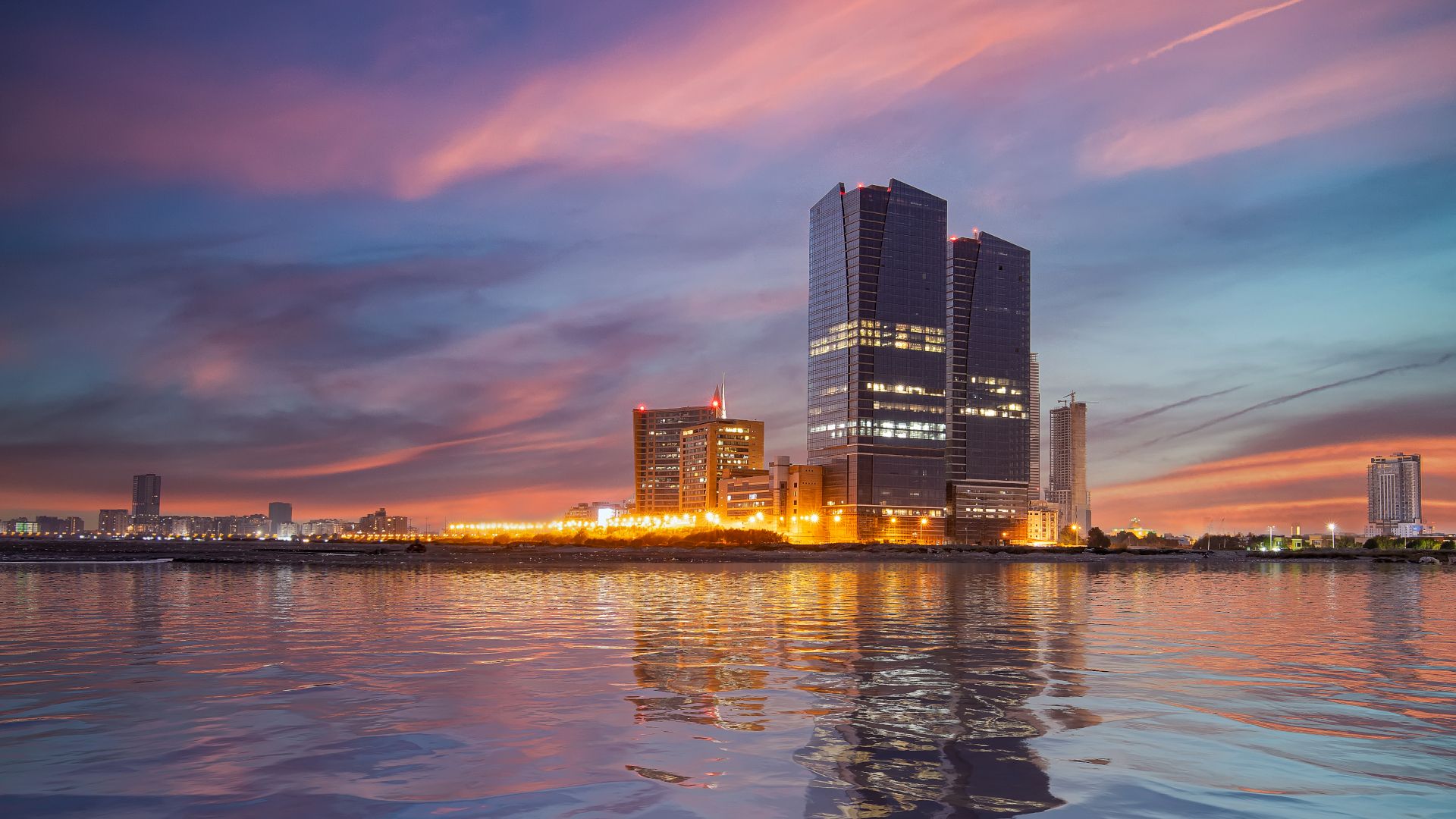 Karachi, Pakistan. In the foreground, the sea reflects the sunset and the base of the Bahria Tower glows with light. 
