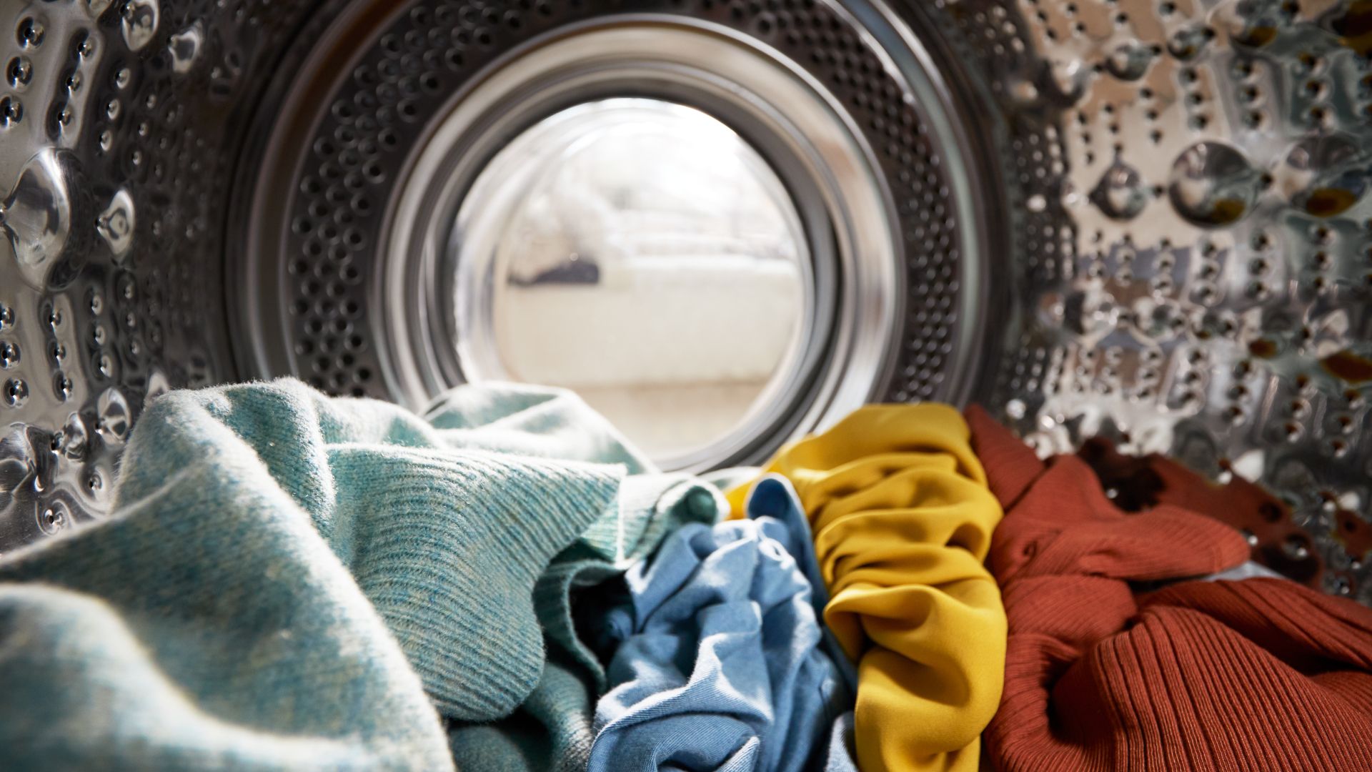 Colourful clothing sitting in the bottom of the drum of a washing machine.
