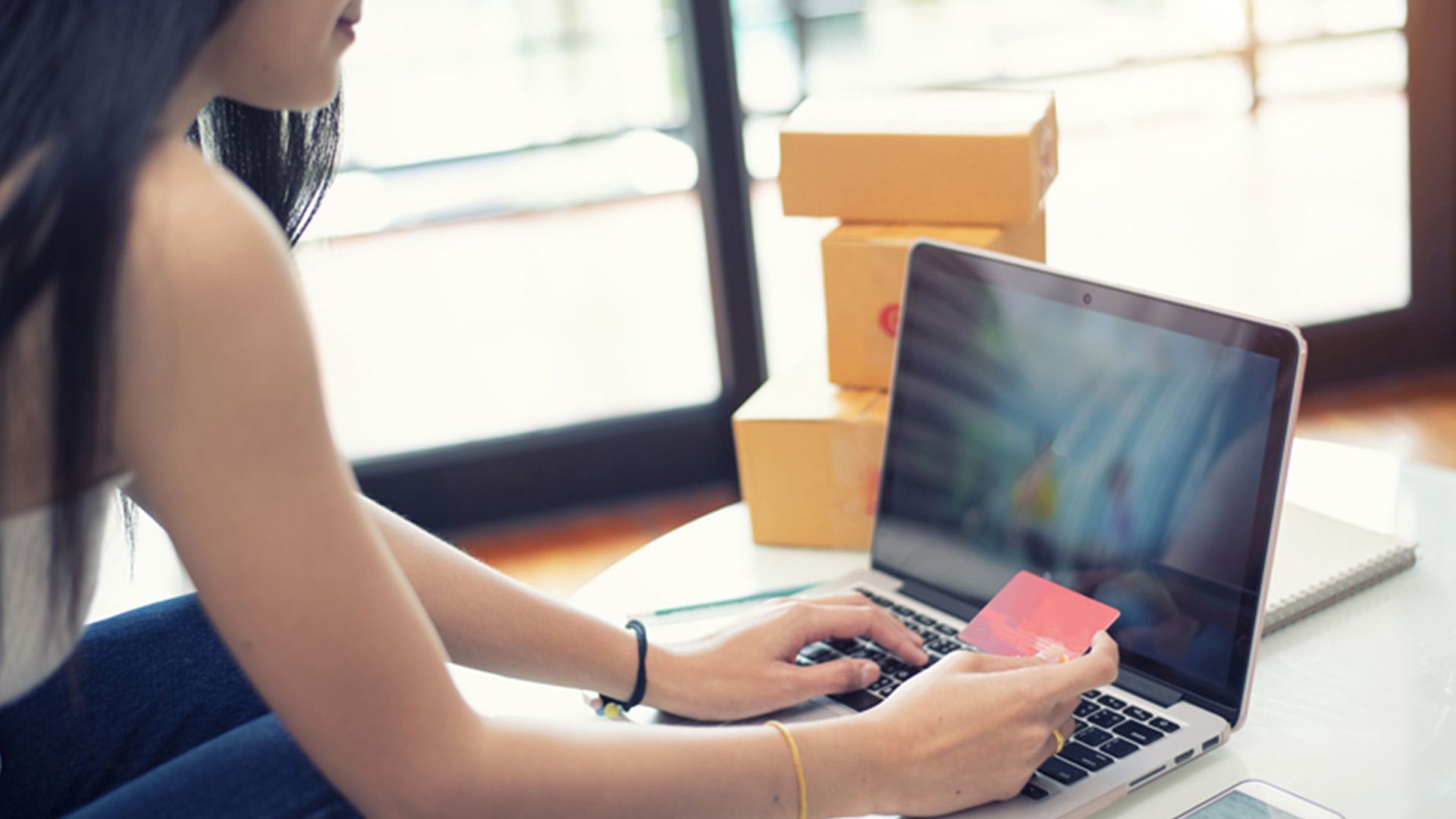 Young woman sitting in front of a laptop and using a credit card to pay for shopping online.