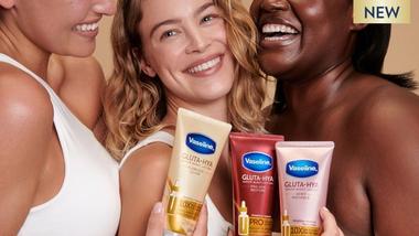 Three women laugh together whilst holding Vaseline products