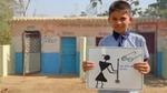 A schoolboy stands in front of a block of toilets holding a hand-drawn poster