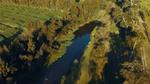 A winding river flows between dense green fields and tall trees in bright afternoon light.