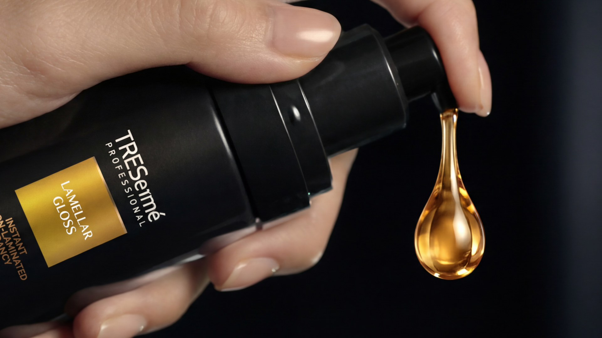 A golden droplet is dispensed by hand from a bottle of TRESemmé Professional Lamellar Gloss Ultra-Gloss Oil. 