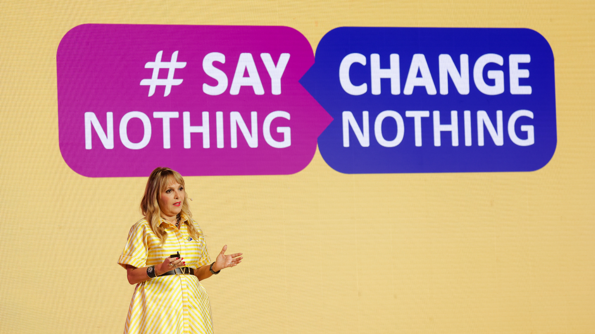 Aline Santos standing on a stage with a background sign with the words ‘Say Nothing, Change Nothing’