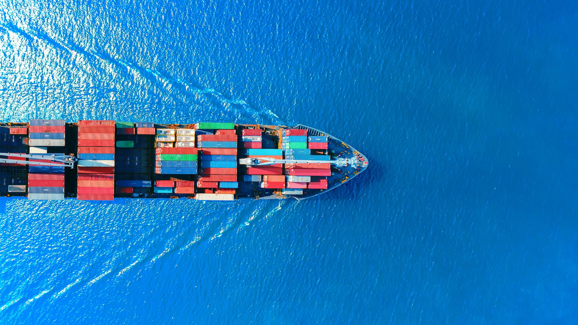 An image of a boat from above, loaded with shipping containers, sailing on open water.