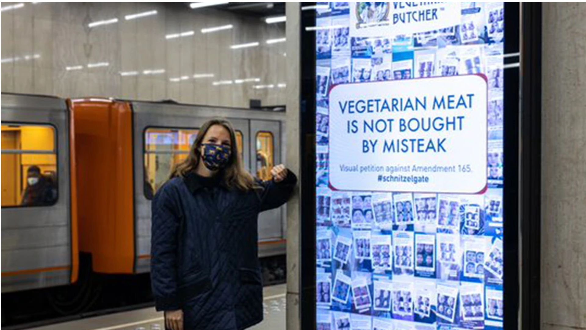 Woman in a face mask in an underground station leaning against a Vegetarian Butcher billboard